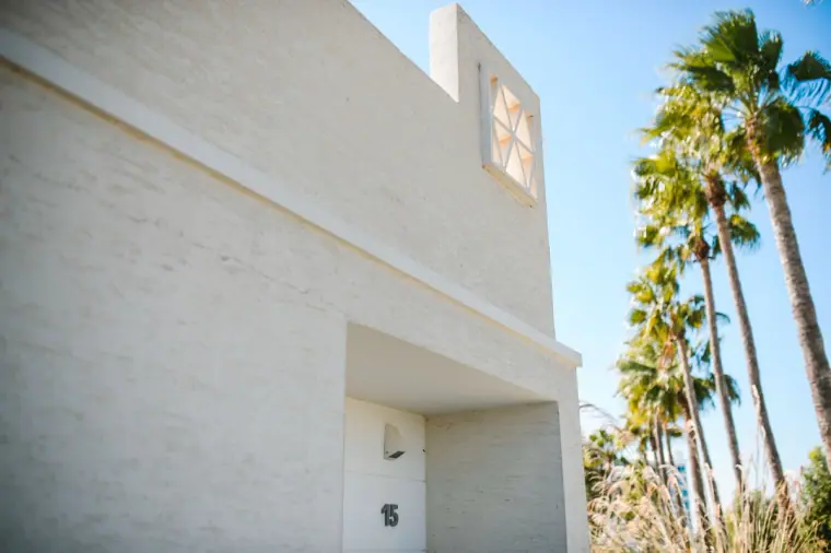 White hotel wall with a room number under palm trees and blue sky