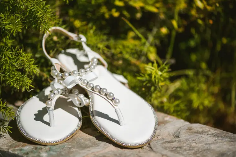 Beaded white bridal sandals on a stone among greenery