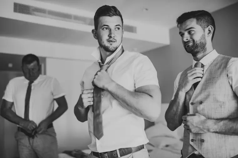 Black-and-white shot of the groom and groomsmen knotting their ties