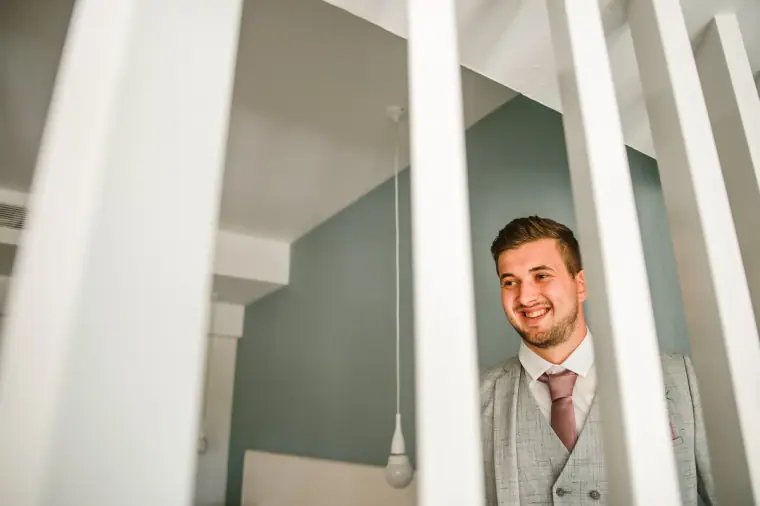 Groom smiling as he peers between white wooden slats