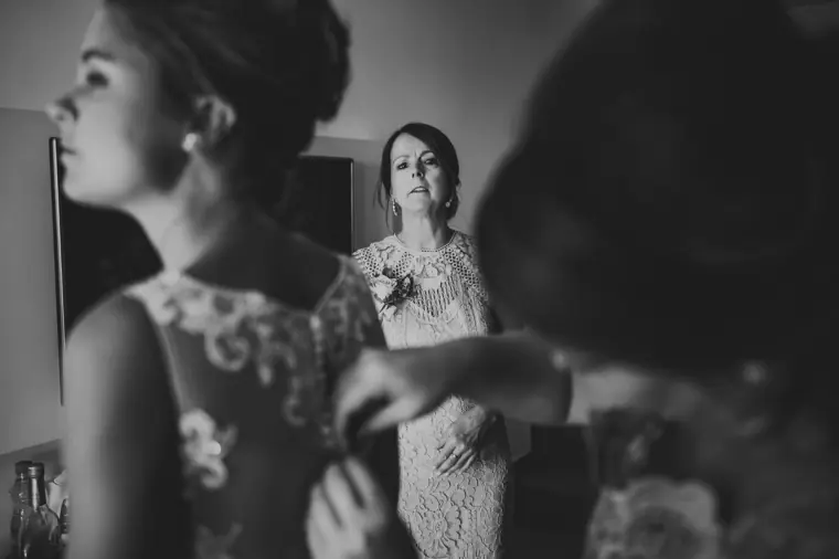 Black-and-white shot of a woman adjusting the bride's lace dress
