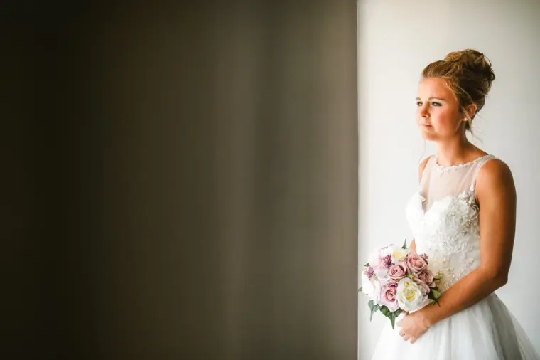 Bride gazing at her bouquet by a bright window