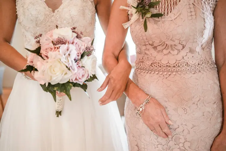 Close-up of the bride's bouquet and a woman in blush lace walking arm in arm