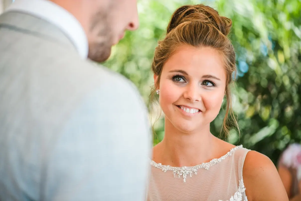Bride smiling at her groom during the ceremony in the hotel gardens