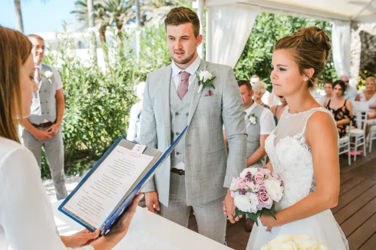 Celebrant reading from a folder as Naomi and Dale stand under the white canopy