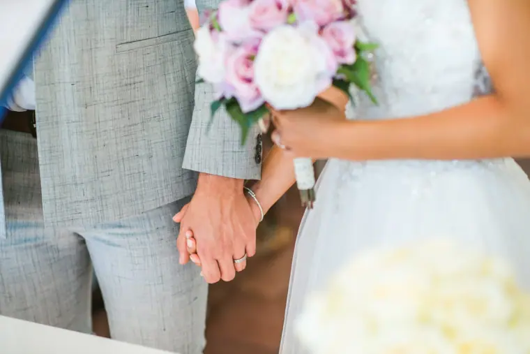 Close-up of the couple holding hands, her pink and white bouquet beside them