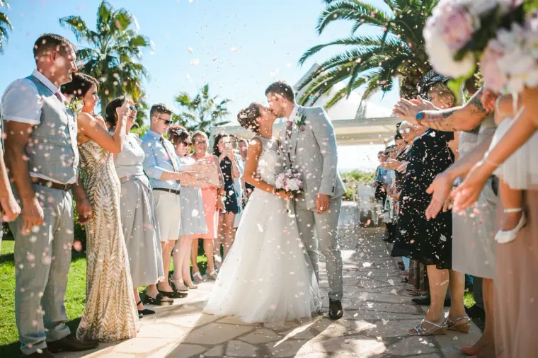 Guests throwing petals as the newlyweds kiss along the garden path