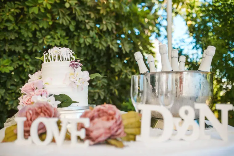 Wedding cake with pink flowers beside LOVE and D&N letters and champagne on ice