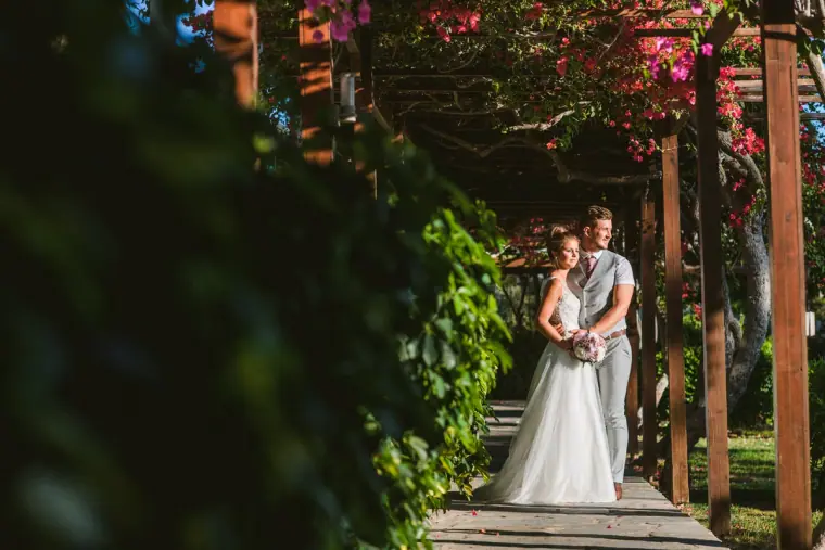 Bride and groom embracing at the end of a flowered wooden walkway