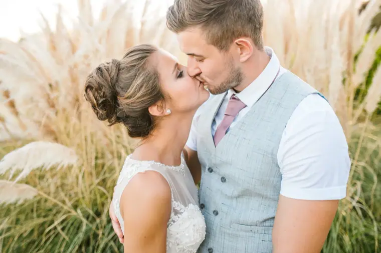 Bride and groom kissing in front of tall pampas grass