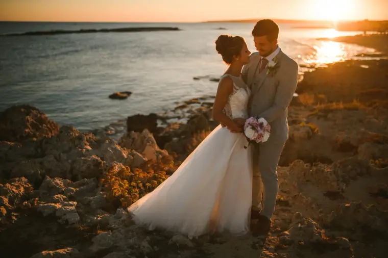 Newlyweds embracing on the rocks as the sun sets over the sea, Ayia Napa