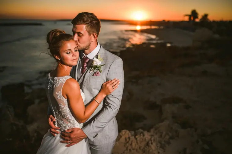 Naomi and Dale embracing as the sun sinks into the sea behind them