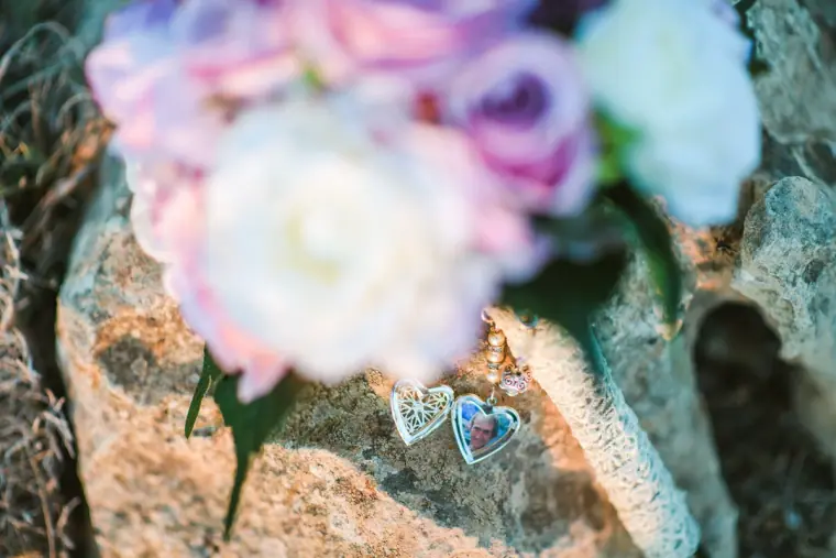 Bridal bouquet and heart-shaped photo lockets resting on a rock