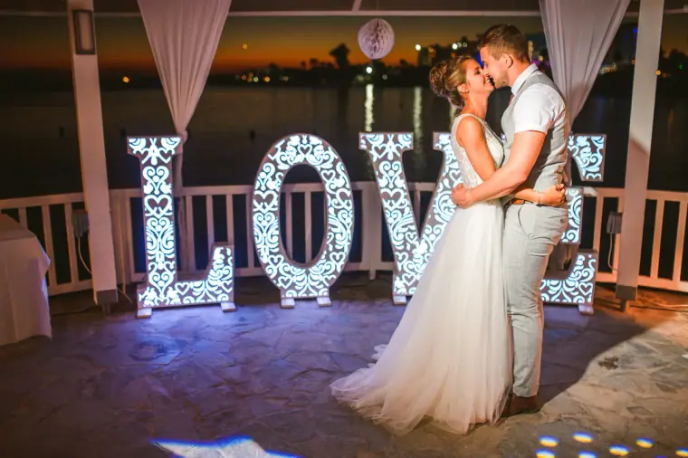 Bride and groom kissing in front of illuminated LOVE letters at night