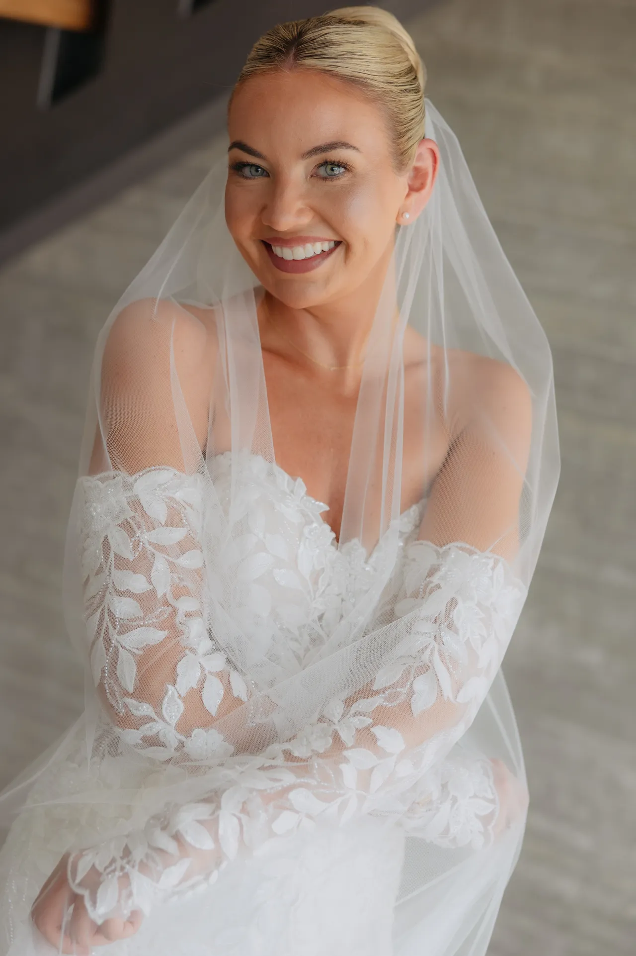 Smiling bride in lace sleeves and veil beside a floating staircase