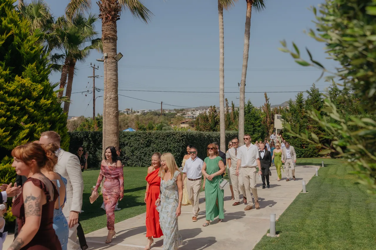 Guests in colourful summer outfits walking along the garden path to the ceremony