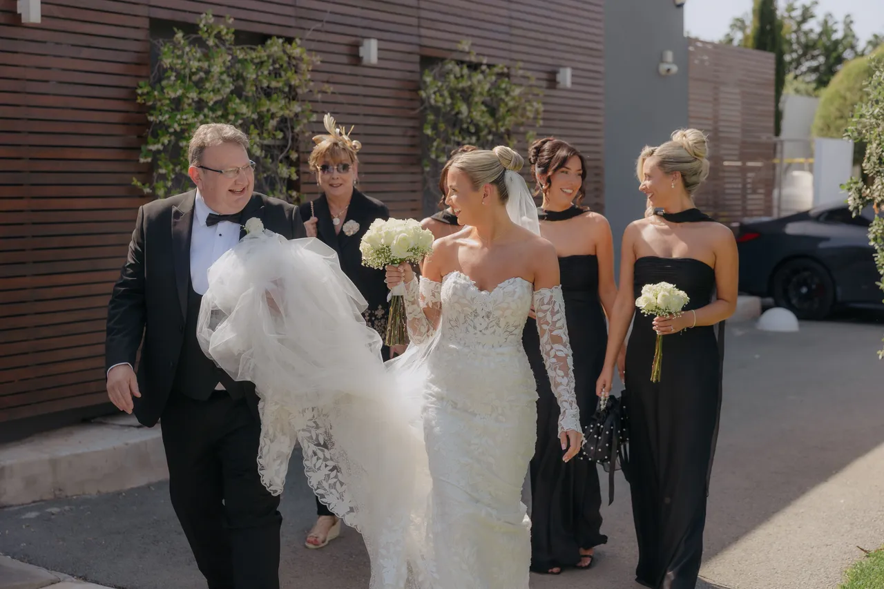 Bride arriving with her father and bridesmaids in black dresses