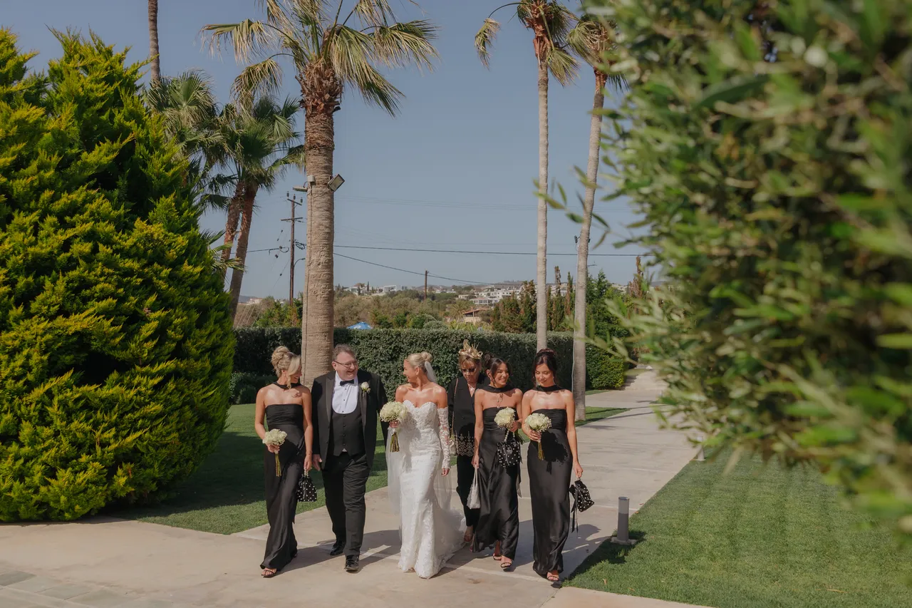 Bride and bridesmaids in black walking the palm-lined path to the ceremony