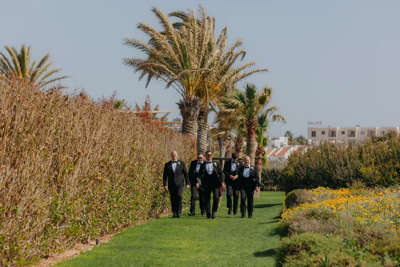 Groom and groomsmen walking across the lawn beside tall grasses and palms