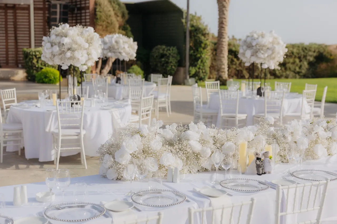 Long reception table dressed with white roses, gypsophila and pillar candles