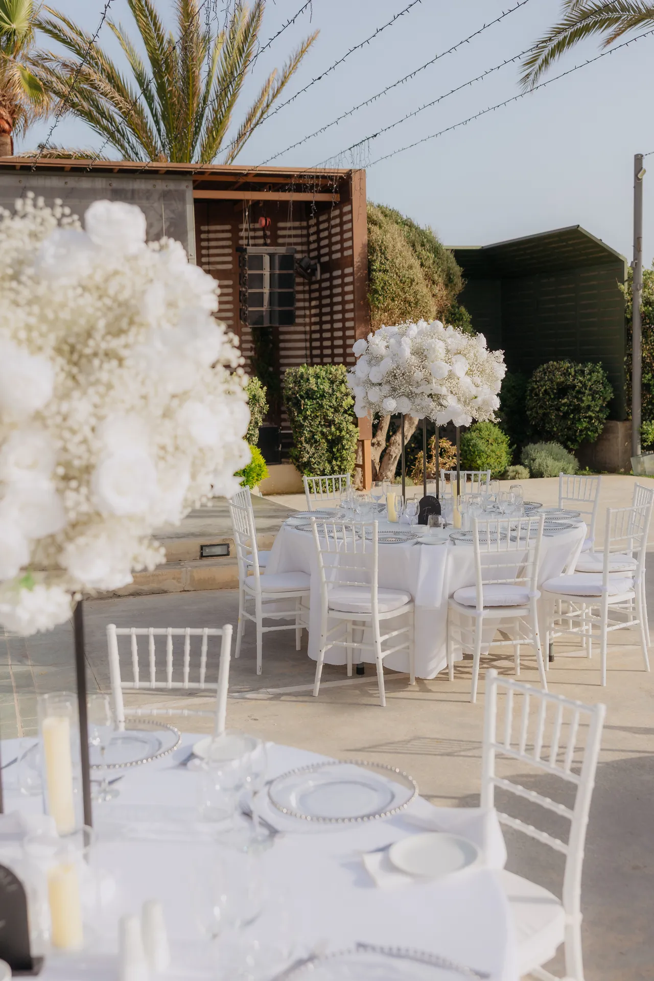 Tall white floral centrepiece above a table set with chiavari chairs