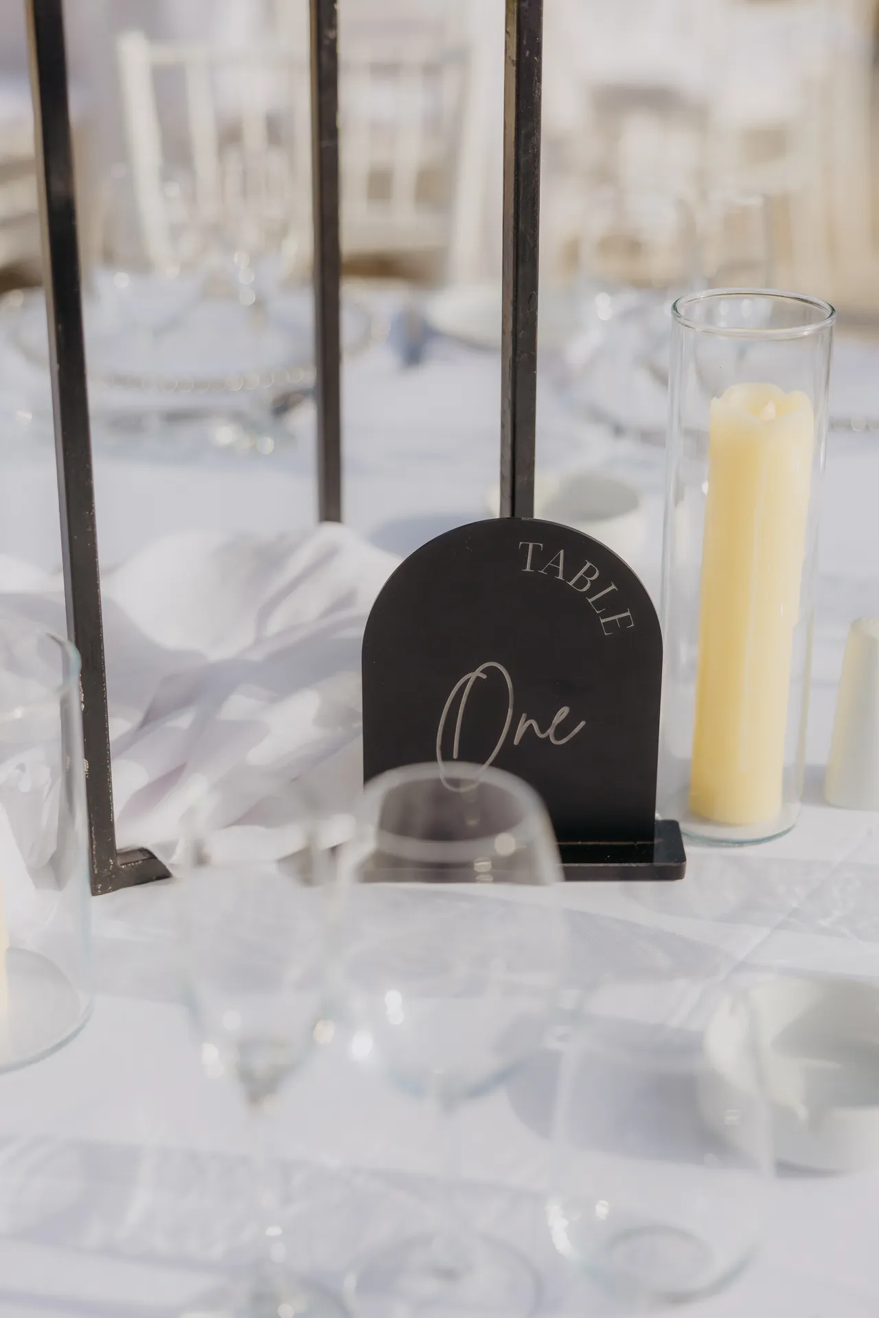 Black arched Table One sign beside a candle and glassware