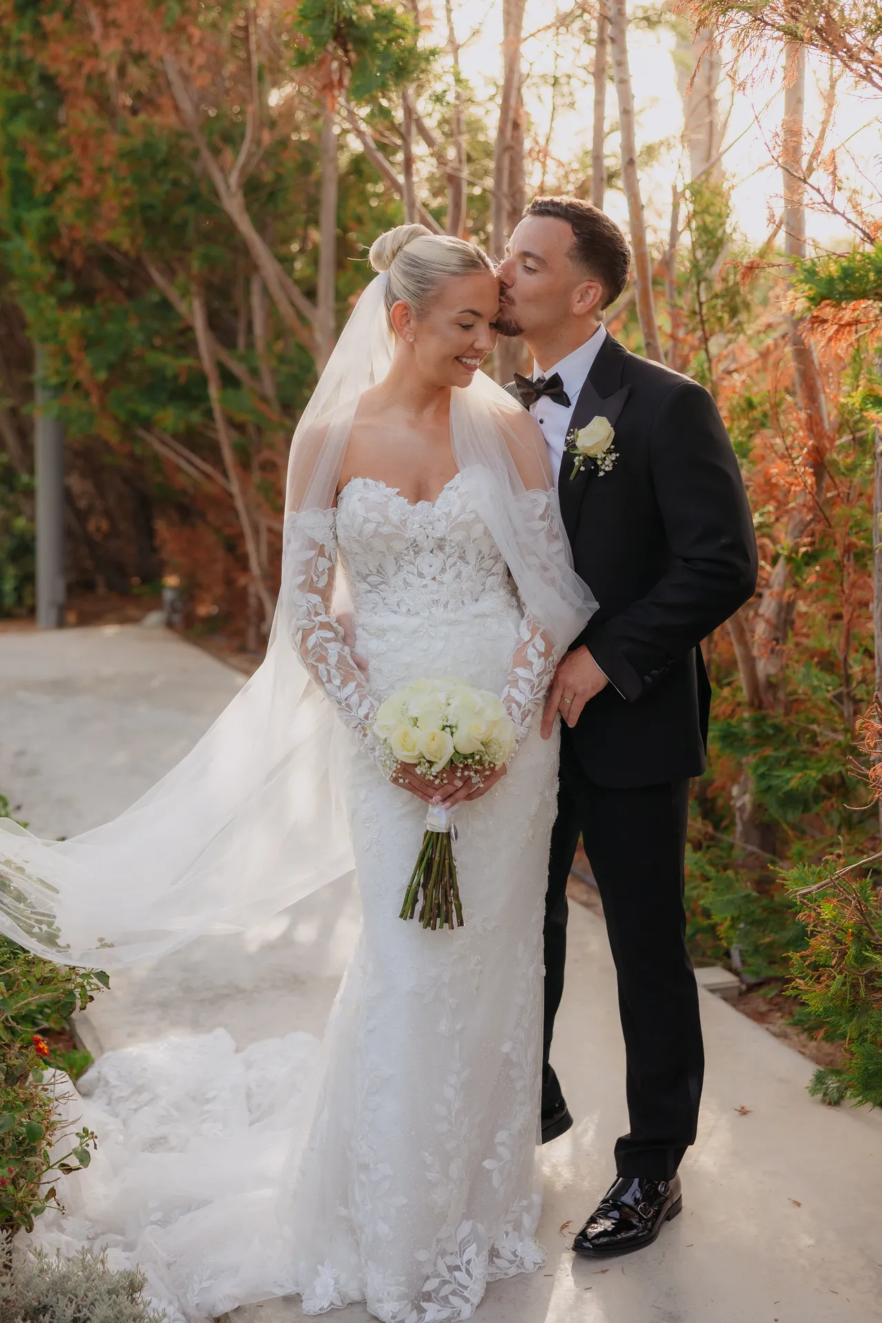 Groom kissing his bride's cheek on a garden path