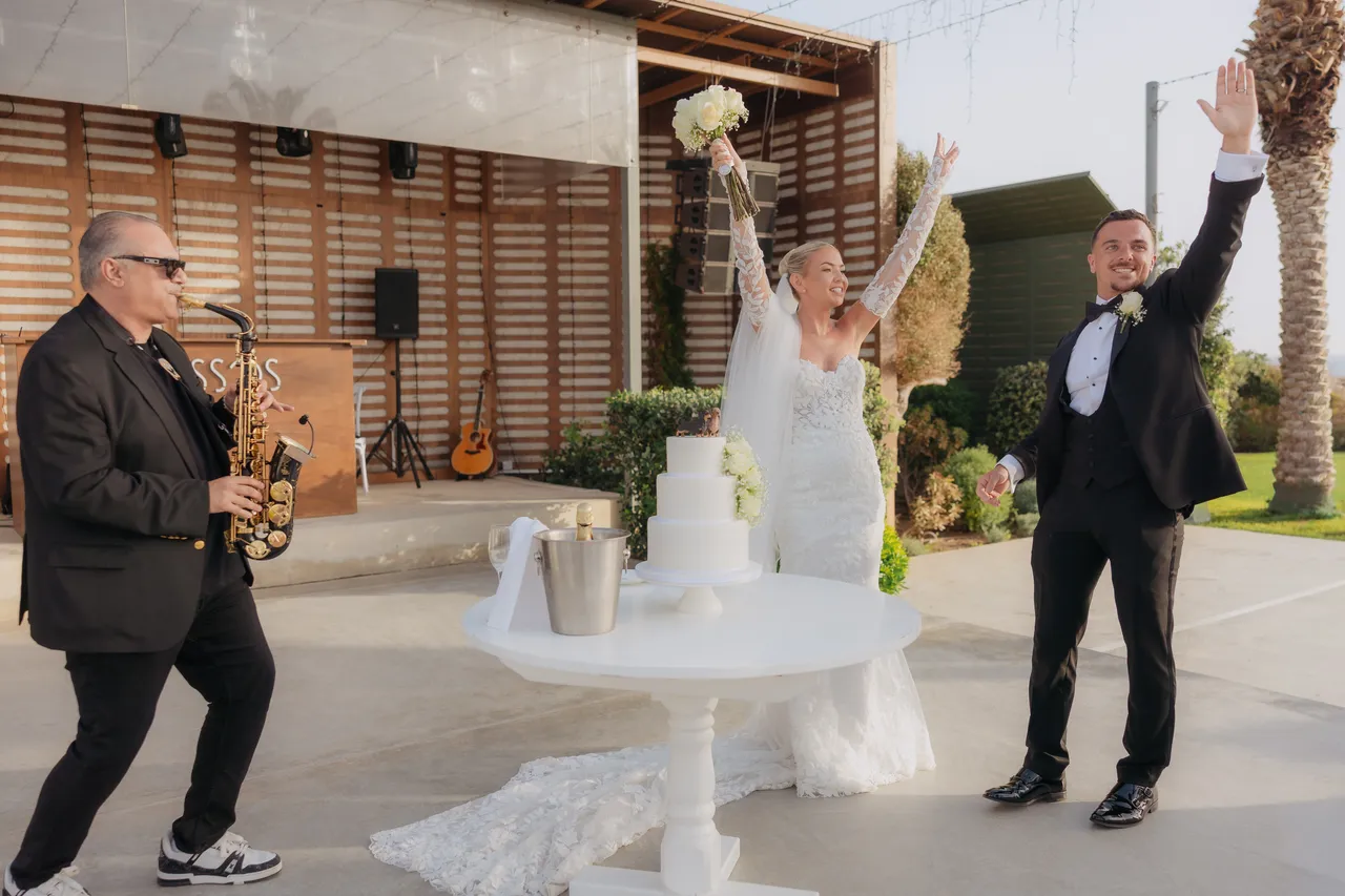 Couple cheering beside the cake table as the saxophonist plays