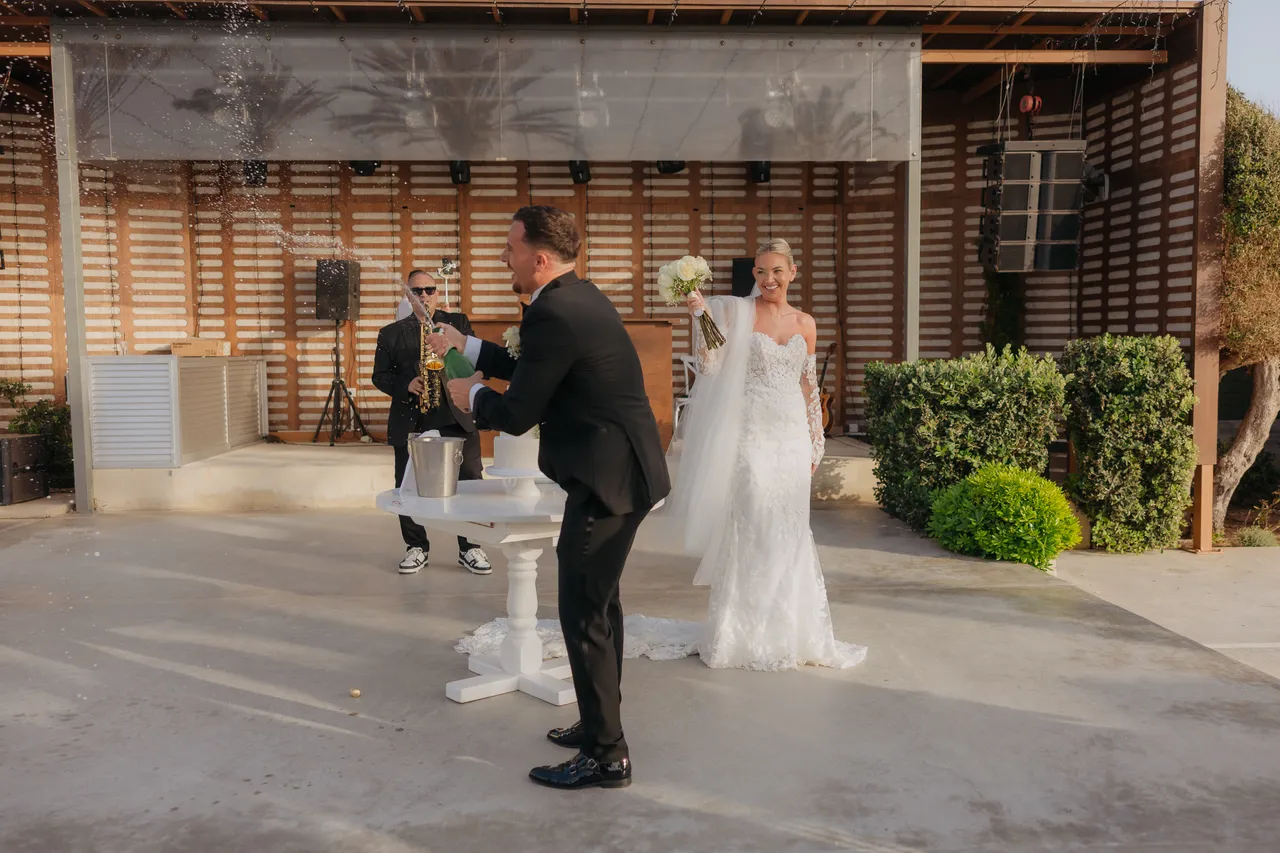 Groom bowing towards his bride beside the cake table