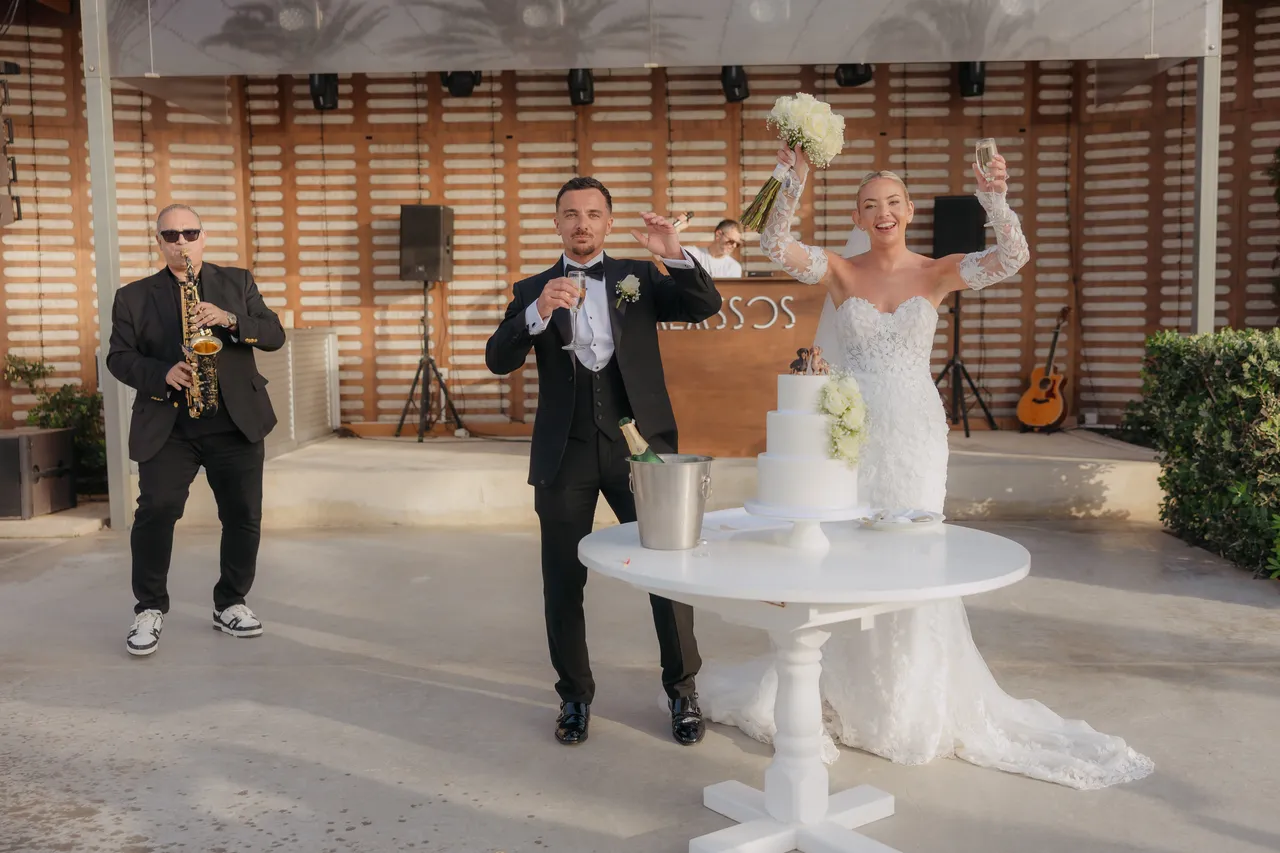 Bride and groom celebrating beside the cake as the saxophonist performs