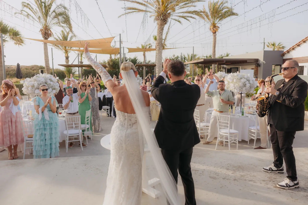 Couple walking through the reception as guests applaud and the saxophone plays