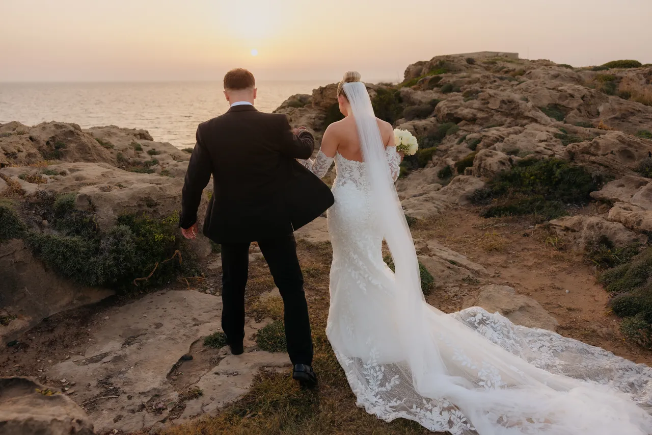 Bride and groom walking over rocks towards the sea at sunset