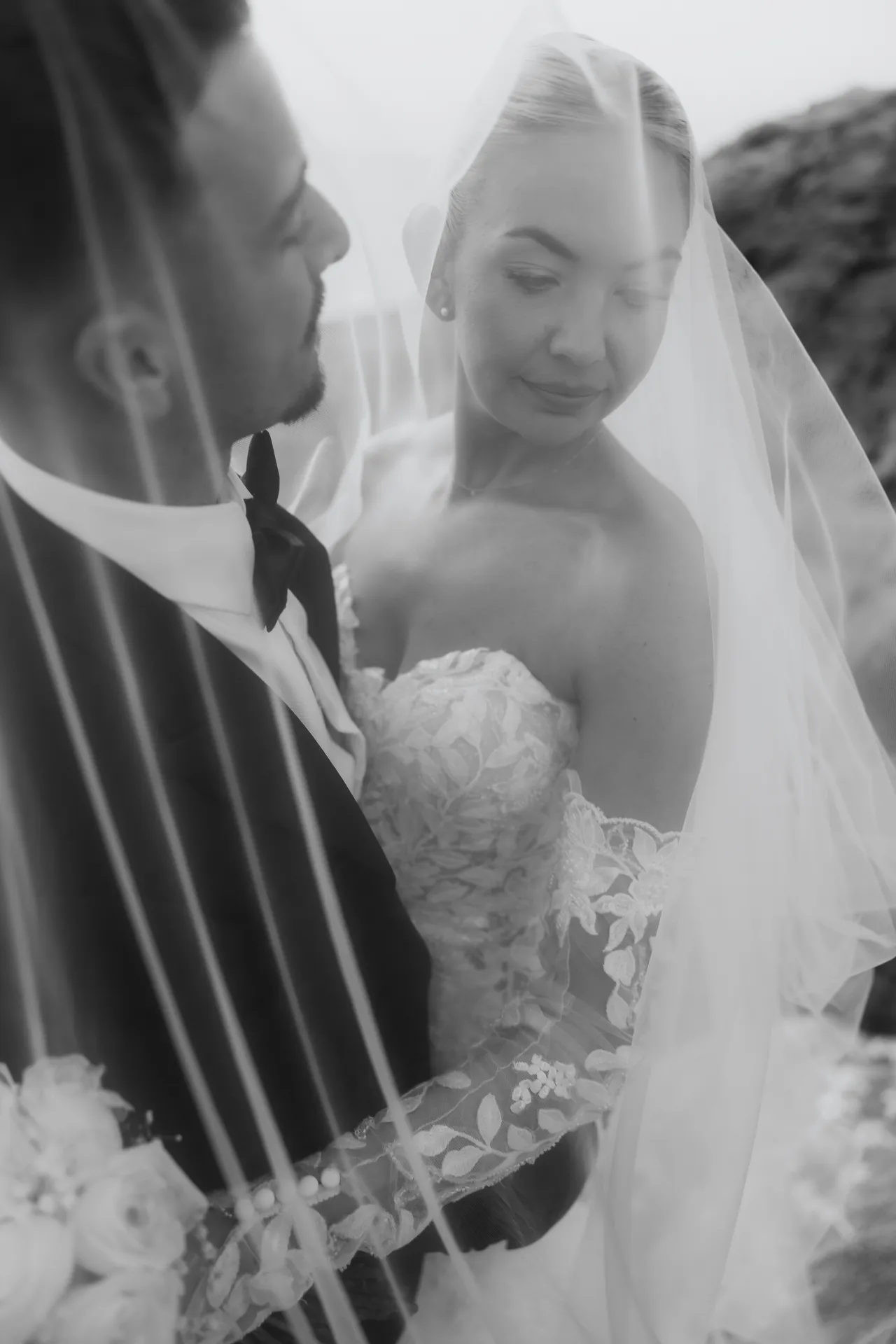 Black-and-white photo of the bride smiling beneath her veil beside the groom