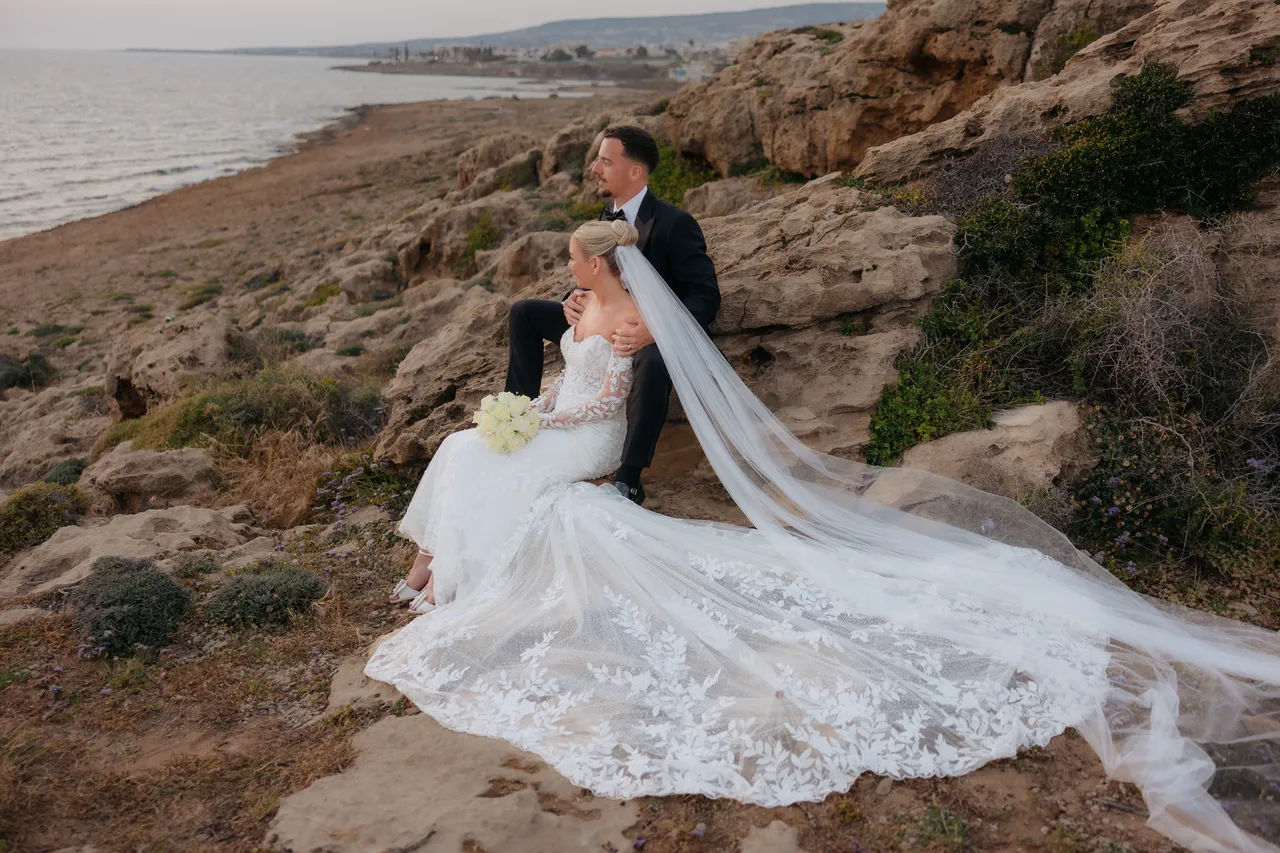 Couple sitting on the rocky coastline with her train and veil spread out