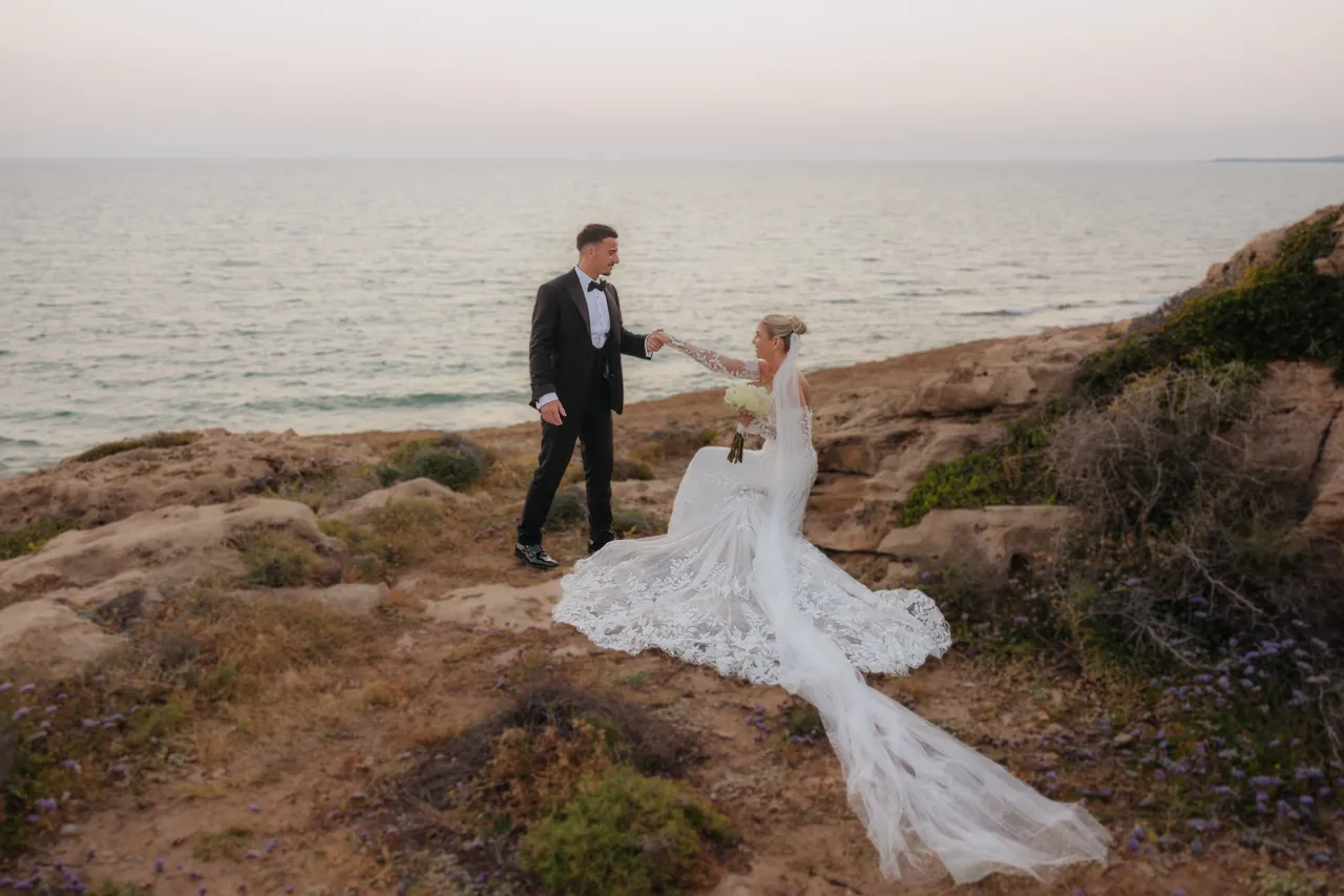 Groom twirling his bride on the clifftop above the sea at dusk