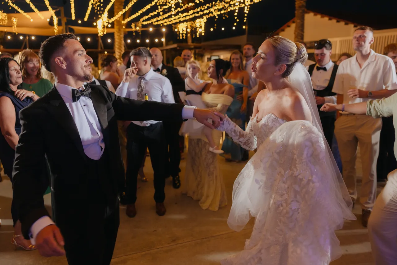 Groom dancing towards his bride under festoon lights