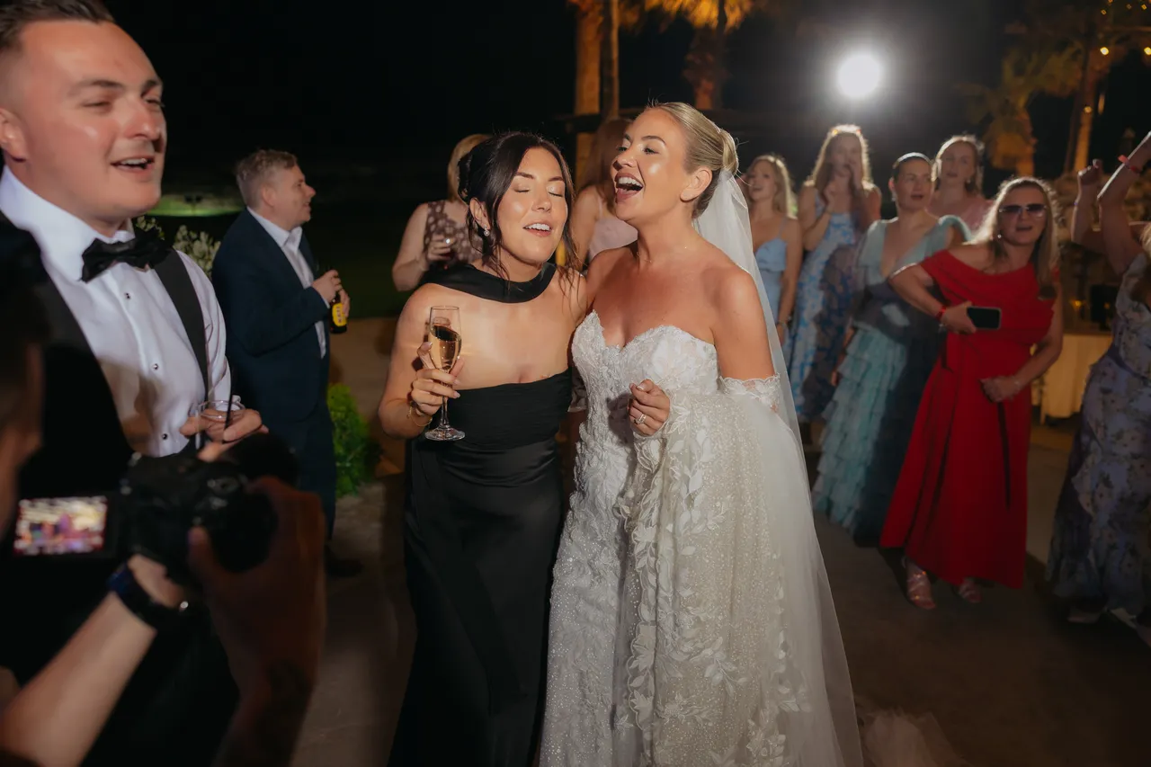 Bride singing along with a friend in a black dress on the dance floor