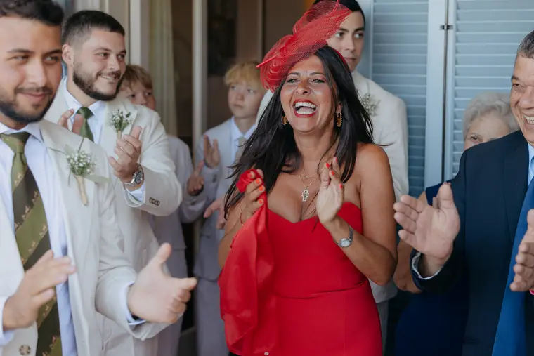 Guest in a red dress and fascinator applauding alongside the groomsmen