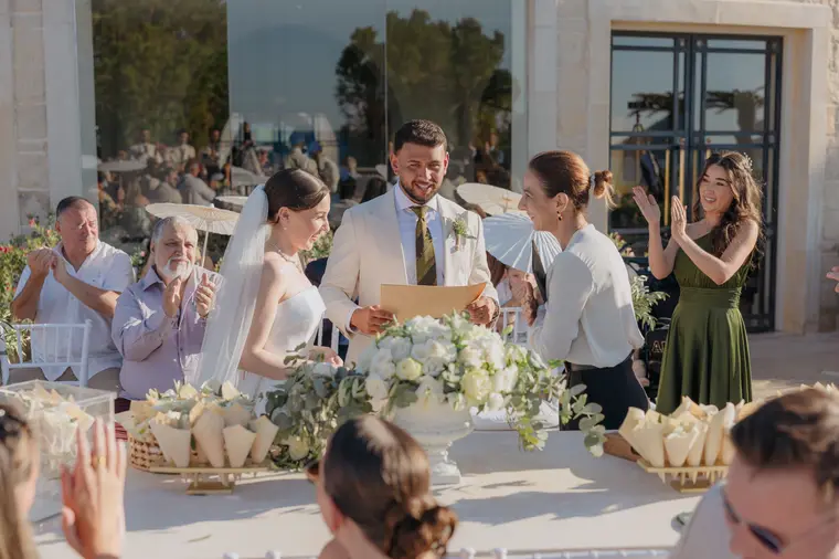 Poppy and Andrew signing their wedding certificate as guests applaud on the terrace
