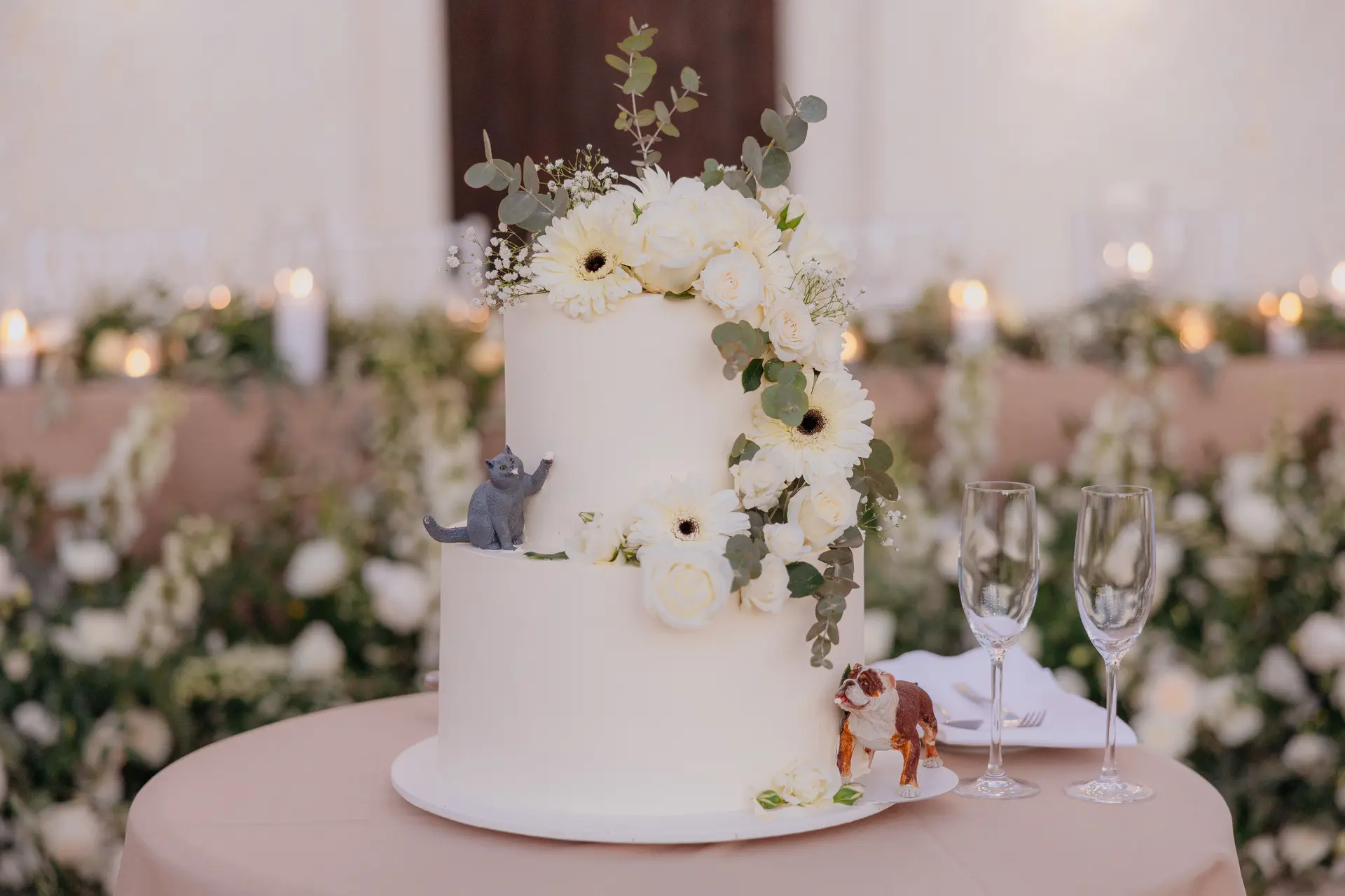 Tiered white wedding cake with white flowers, greenery and two small animal figurines