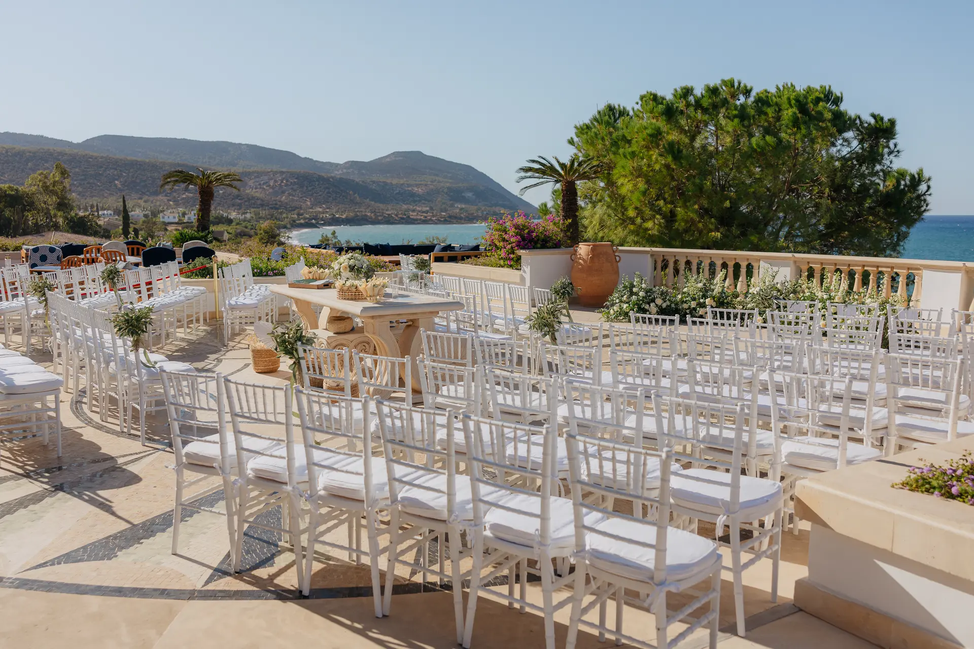Rows of white chairs set on the terrace for the ceremony, sea and hills beyond, at Anassa