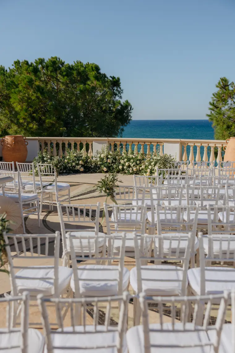 Empty ceremony aisle of white chairs leading to the balustrade and the sea