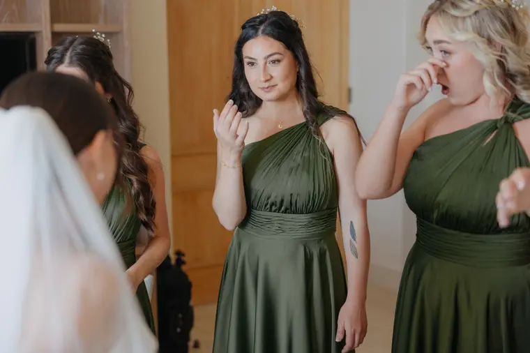 Bridesmaids in green satin dresses wiping away tears as the bride gets ready