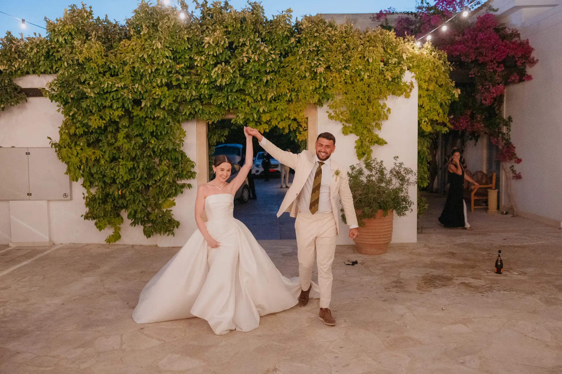 Poppy and Andrew dancing beneath a greenery-covered archway in the evening