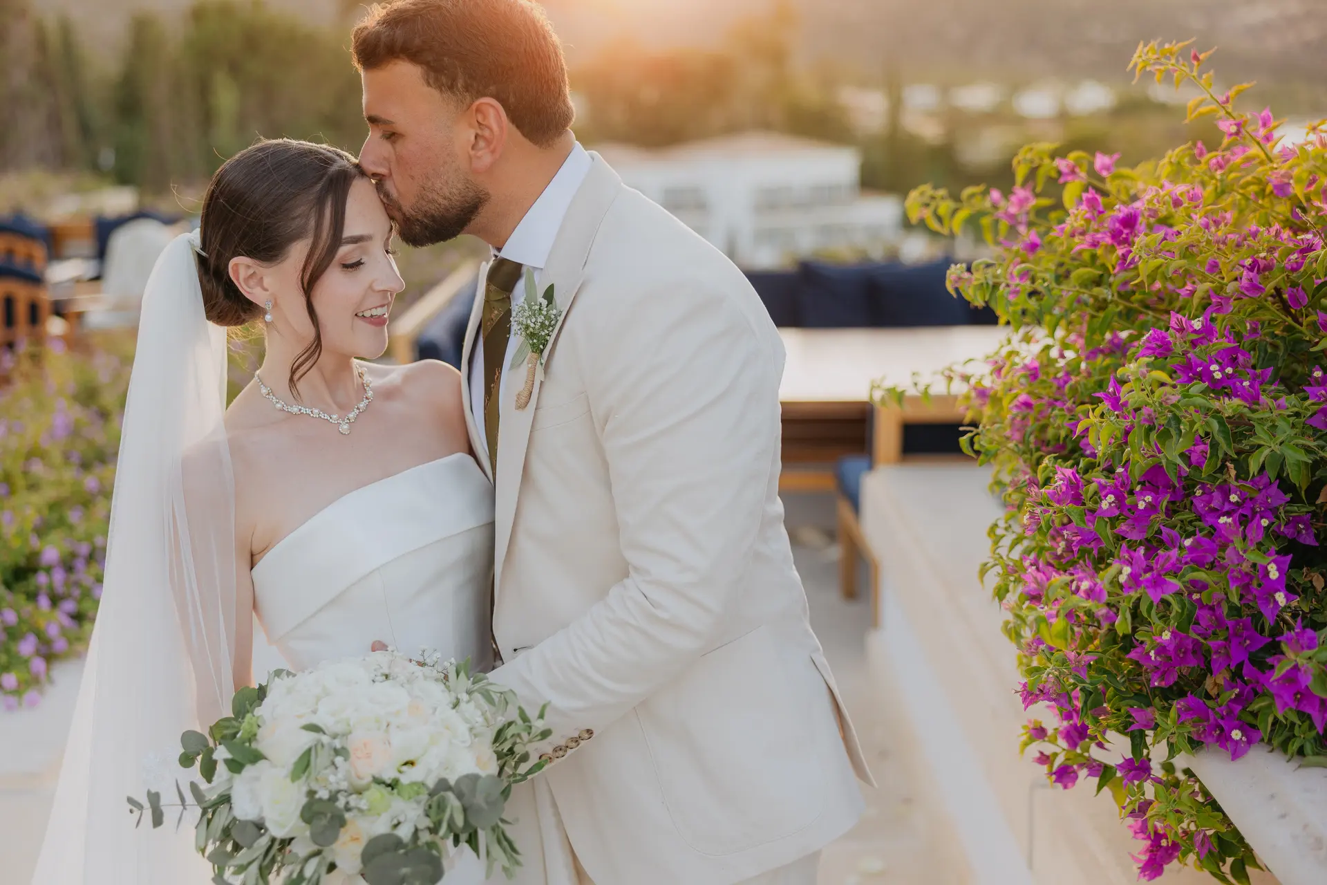 Andrew kissing Poppy's forehead beside pink bougainvillea