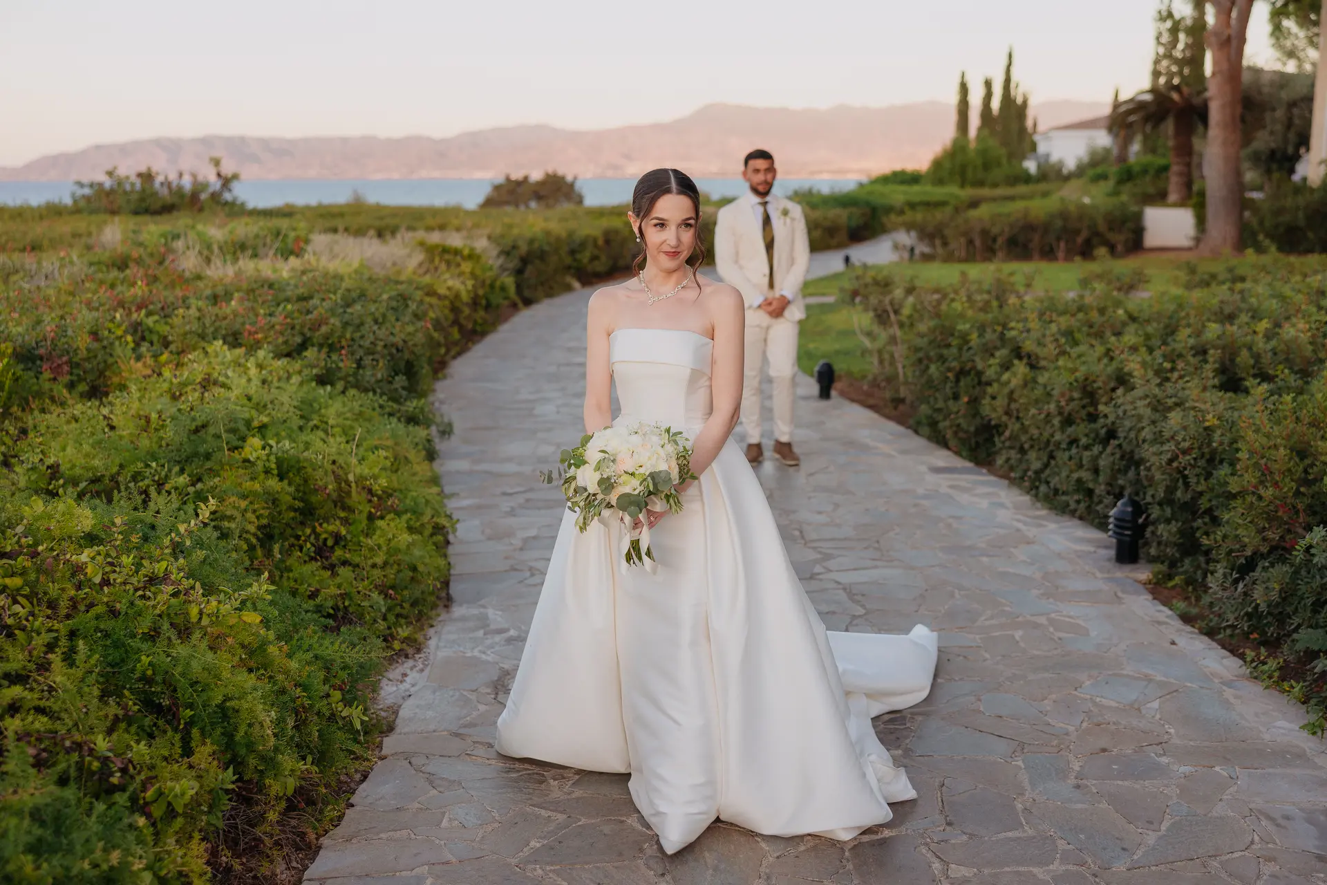 Poppy holding her bouquet on a stone garden path, Andrew behind her