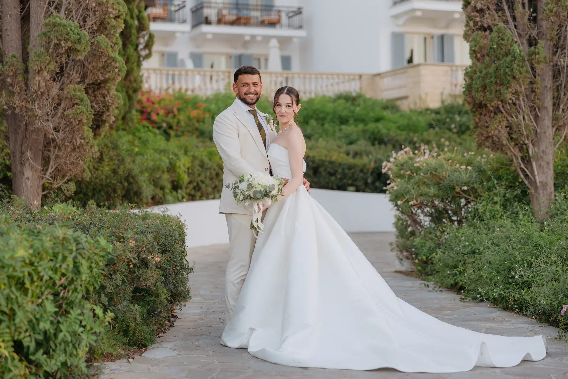 Bride and groom together on a garden path in front of Anassa's buildings