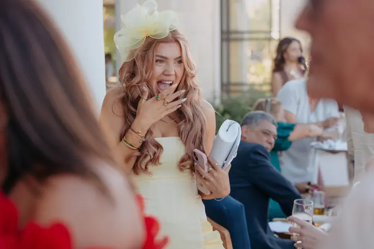 Guest in a yellow dress and fascinator laughing during the cocktail hour at Anassa