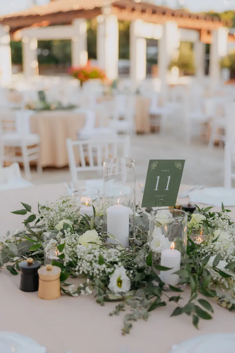 Candlelit centrepiece of white flowers and greenery with a green table number