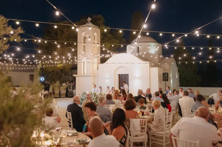 Guests dining in front of the floodlit white chapel beneath string lights